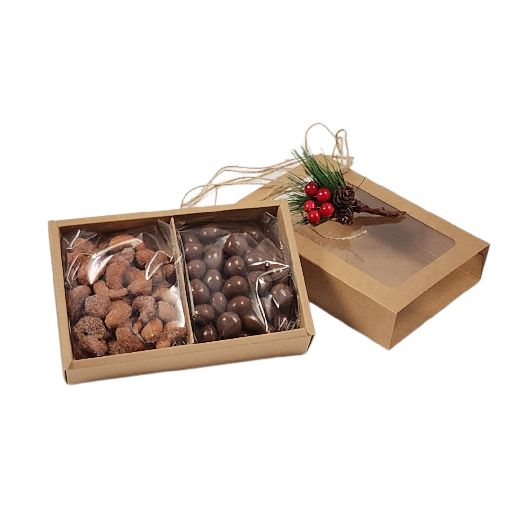 divided kraft slider box with lid off showing chocolate pretzel balls and honey roasted cashews, twine and sprig of pine to the side