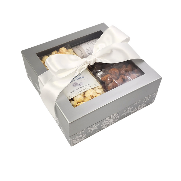 Let It Snow Snack Gift Box featuring artisanal popcorn, honey roasted cashews, and more, elegantly wrapped with a white ribbon for holiday gifting.