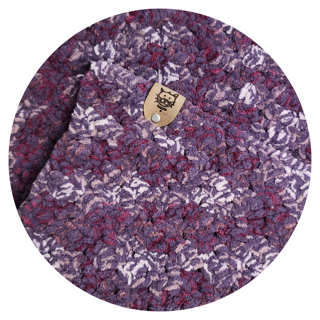 COZY CRASH PAD - PERSIAN PLUM: A plush, purple crocheted cat pad with a leather tag, featuring a cat drawing, ideal for protecting furniture or lining carriers.